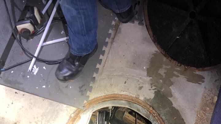 A circular opening in a concrete floor reveals a ladder leading to a hidden underground area