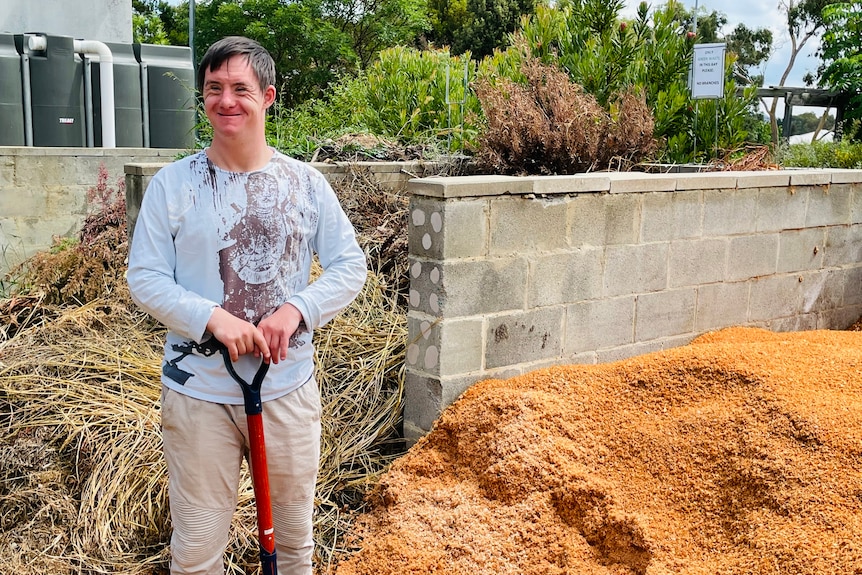 A man stands holding a shover next to a large pile of sawdust