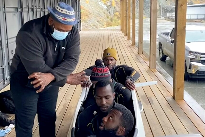 Coach speaks with four athletes sitting in a bobsled