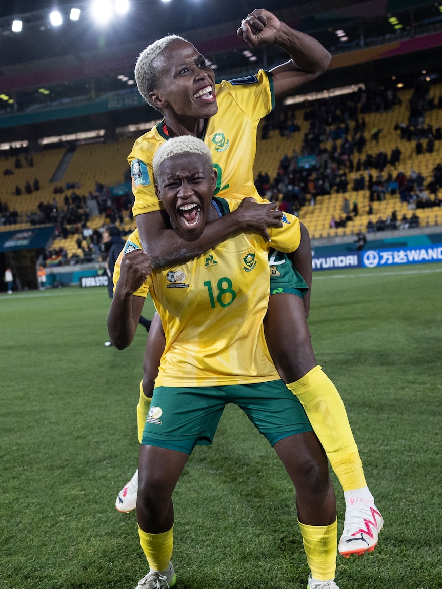 Two soccer players wearing yellow and green celebrate after winning a game