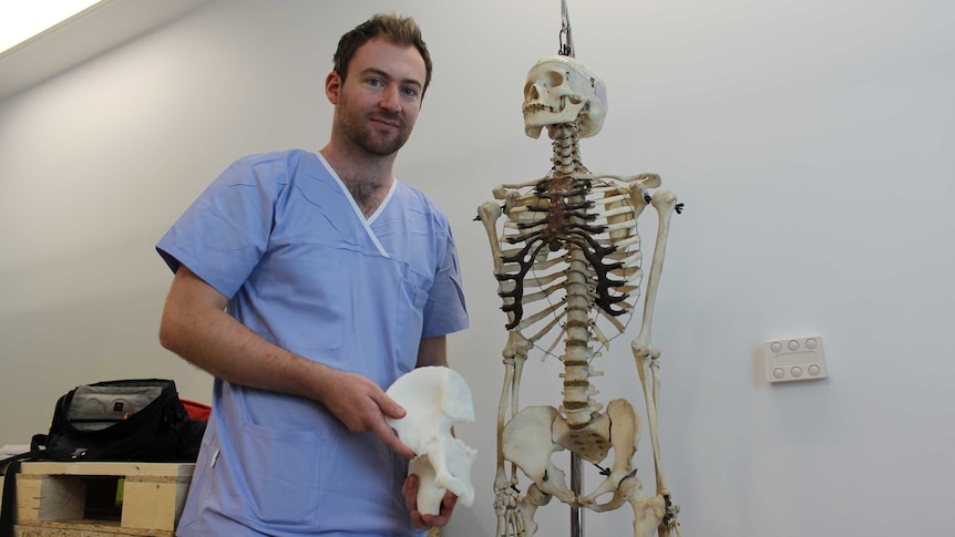 Orthopaedic surgeon Dr Jonathan Davis holds a 3D printed pelvis bone next to a human skeleton.