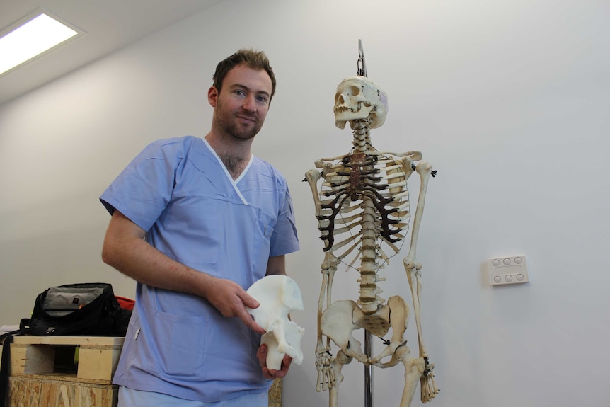 Orthopaedic surgeon Dr Jonathan Davis holds a 3D printed pelvis bone next to a human skeleton.