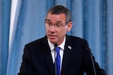 Mark Regev stands at a pdoium