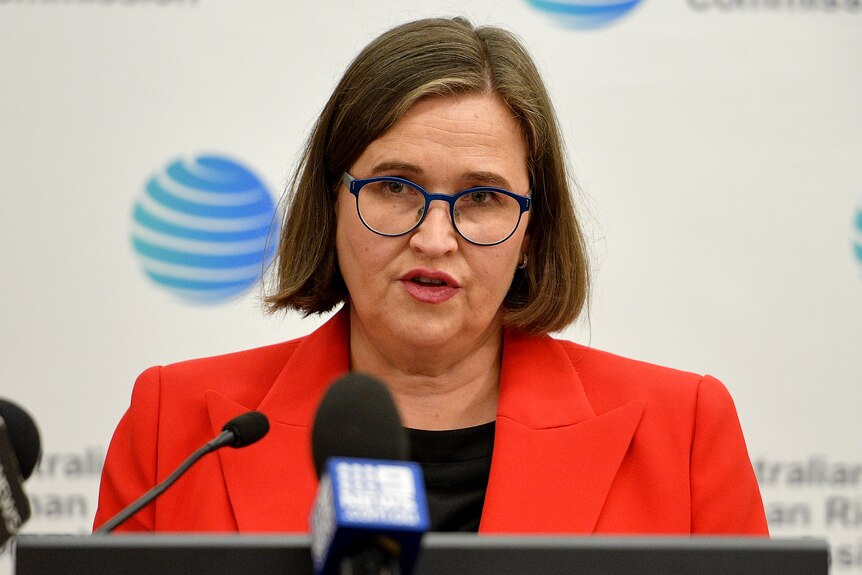 une femme portant des lunettes parlant dans des microphones lors d'une conférence de presse