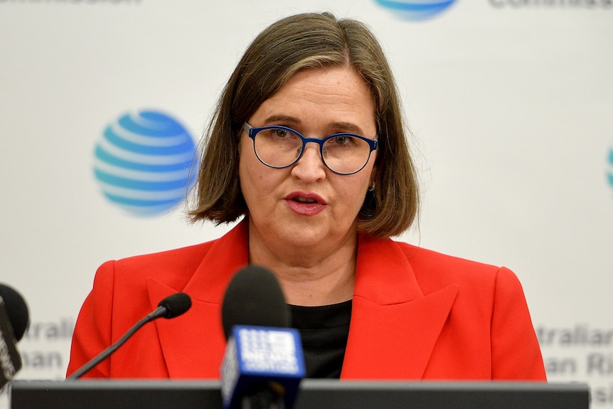 a woman wearing glasses talking into microphones at a press conference
