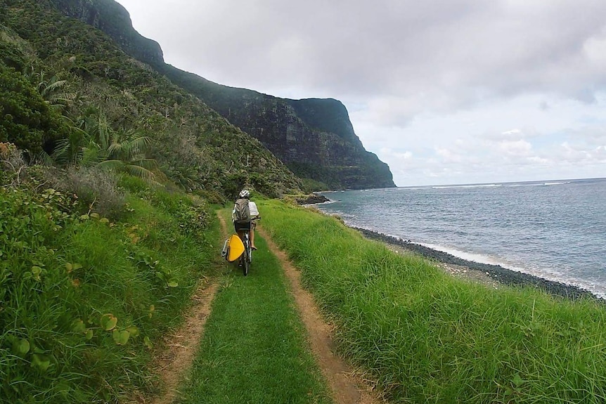 A person rides a bike along an idyllic dirt track next to a beach.