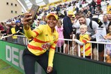 Australian cricketer Alana King has a big smile as she holds her phone in front of her with Trent Rockets fans behind her.