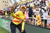 Australian cricketer Alana King has a big smile as she holds her phone in front of her with Trent Rockets fans behind her.