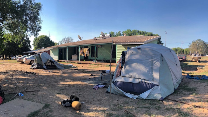 Four cars and two tents in the yard of a green house in Maningrida