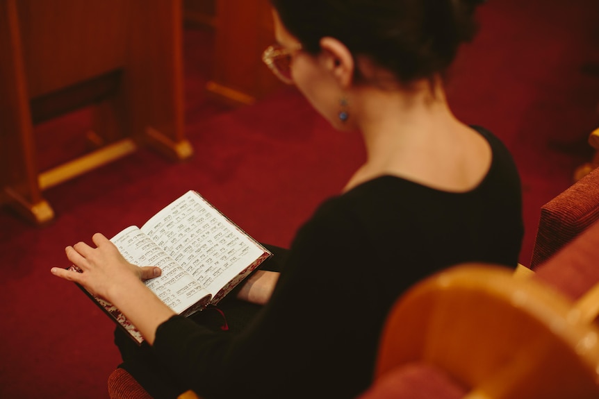 Over the shoulder shot of Nicky Gluch holding and reading a Jewish prayer book.