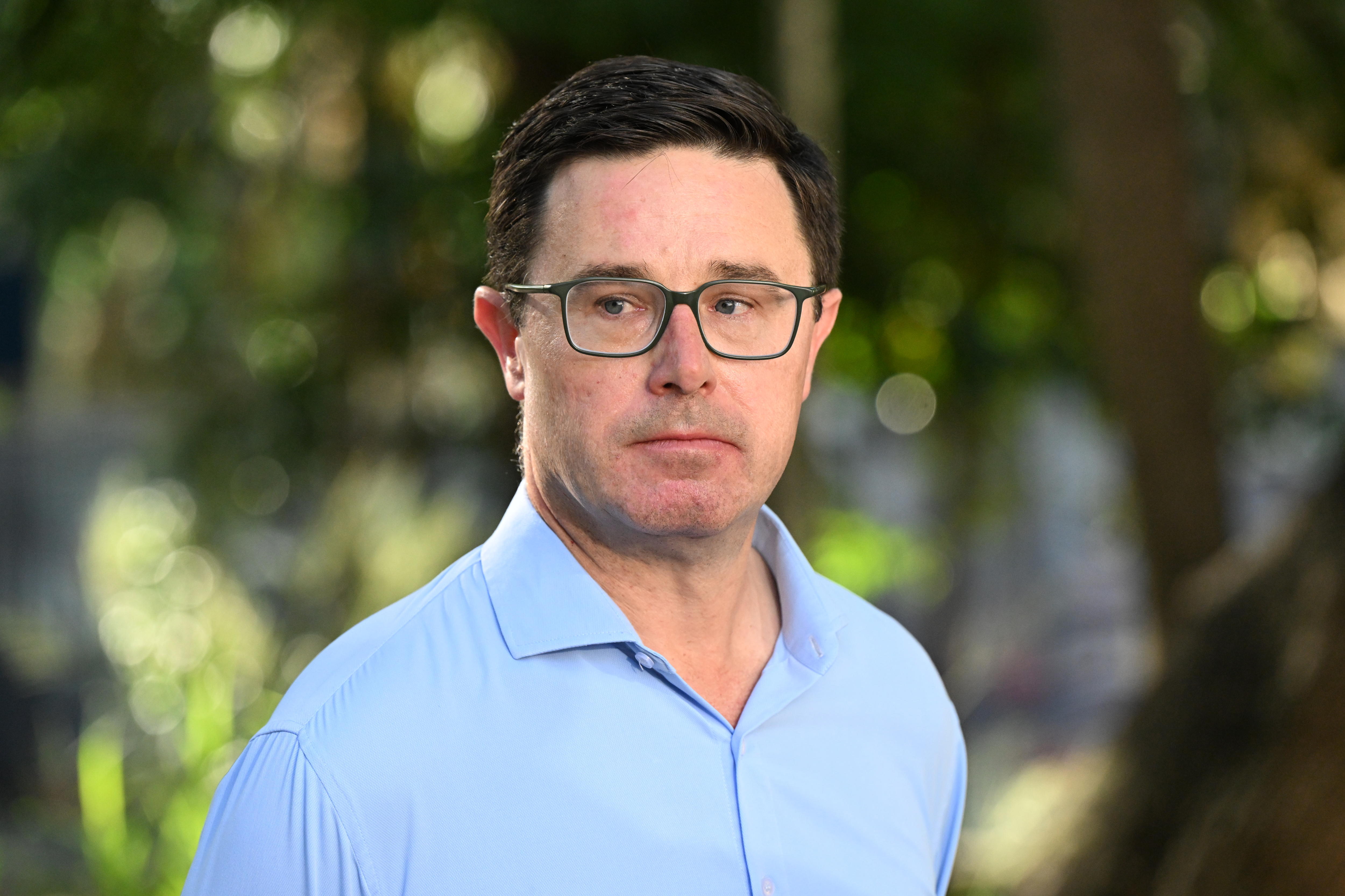 Un primer plano de un hombre con una camisa azul parado afuera.