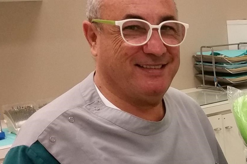 A smiling man wearing glasses and dental scrubs