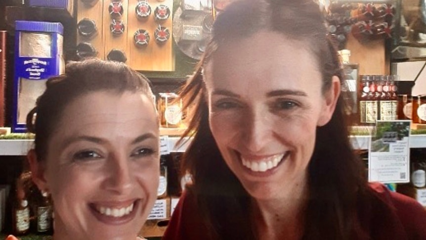 Two women smile at the camera in front of a cheese display.