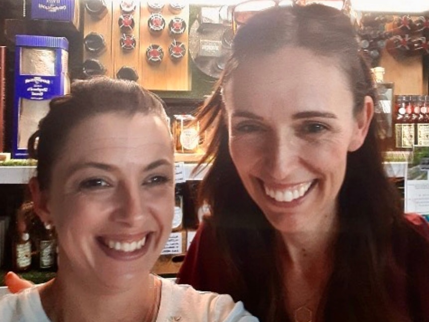 Two women smile at the camera in front of a cheese display.