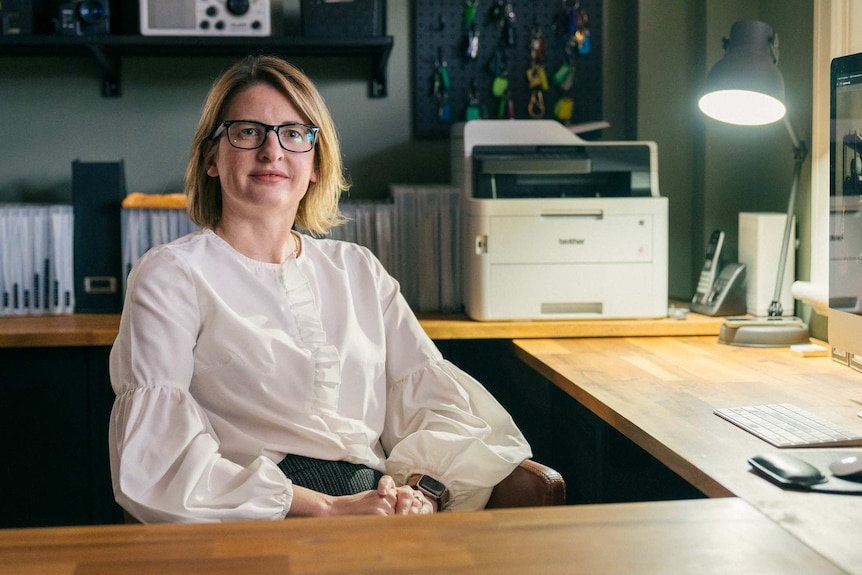 Woman sitting at office desk wearing glasses with bright lamp behind her. 