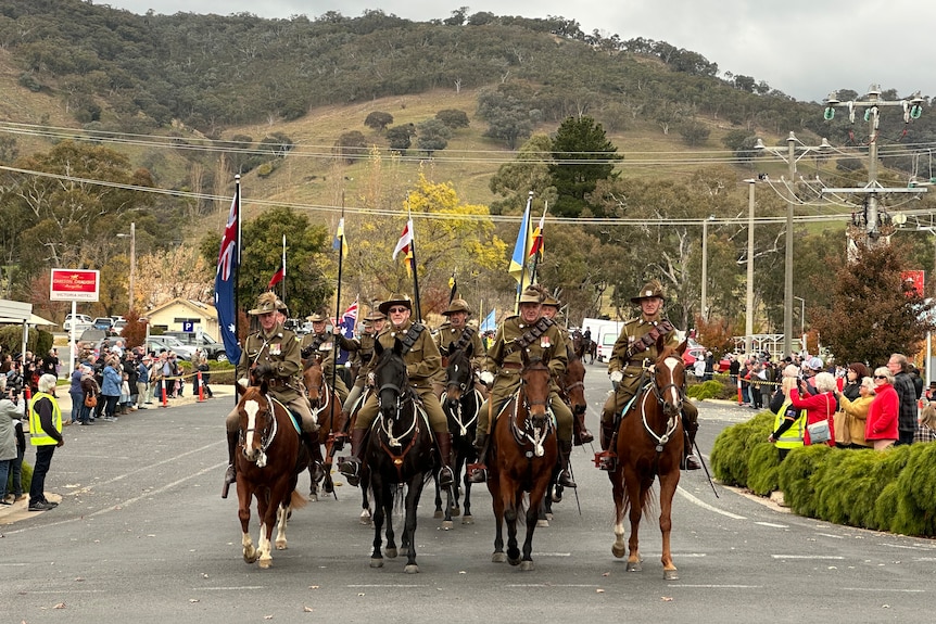Photo of a group of men in uniforms on horseback riding down a street.
