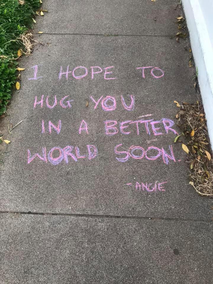 The words 'I hope to hug you in a better world soon' written in chalk on a footpath.