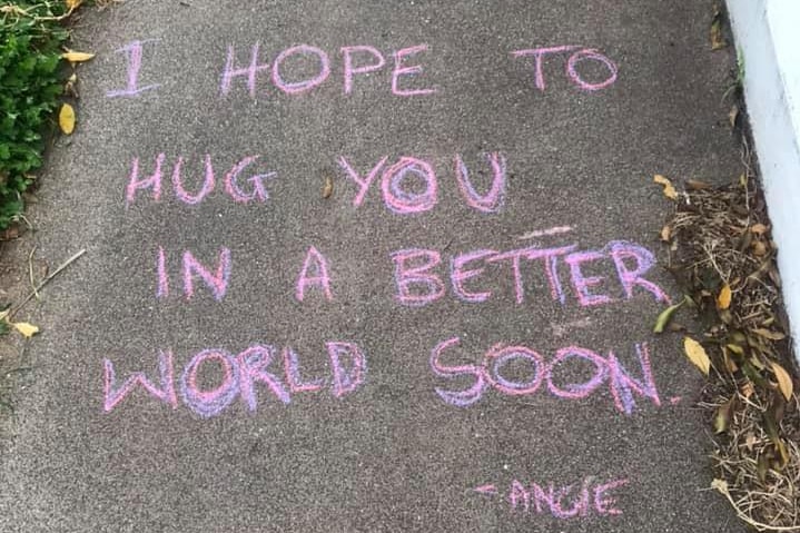 The words 'I hope to hug you in a better world soon' written in chalk on a footpath.