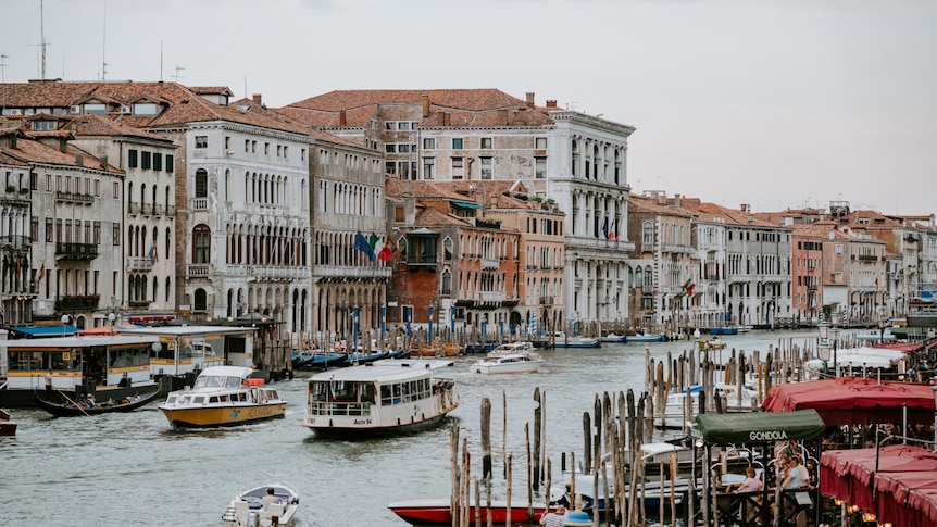 Looking across the canal, with gondalas and boats, to a line of Venetian buildings.