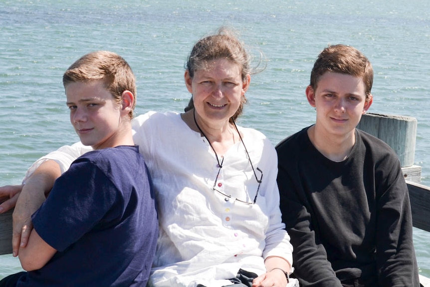 A woman sits between two young men, water in background.