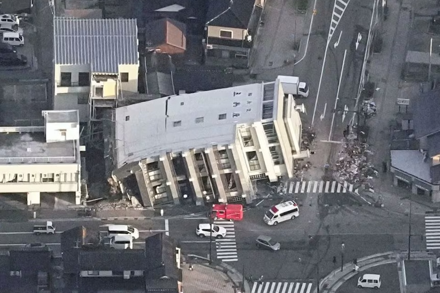 A collapsed building in the middle of a road with cars surrounding it 