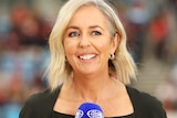 Liz Ellis smiles while holding a microphone courtside