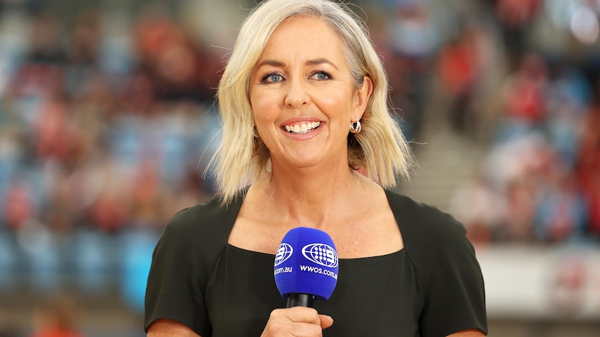 Liz Ellis smiles while holding a microphone courtside