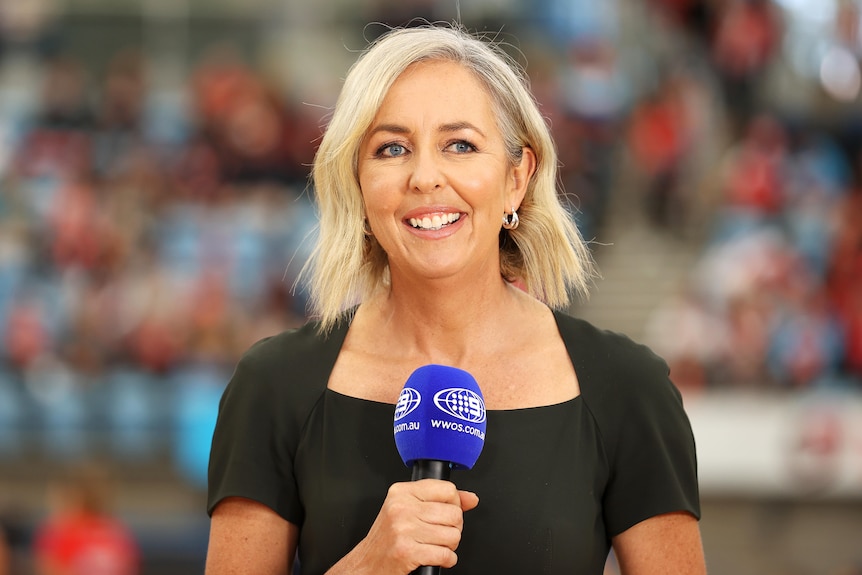 Liz Ellis smiles while holding a microphone courtside