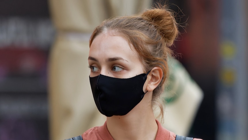 Young woman wearing a mask in outdoor setting.