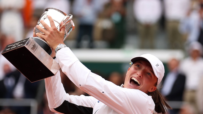 A woman smiles as she lifts a trophy in the air.