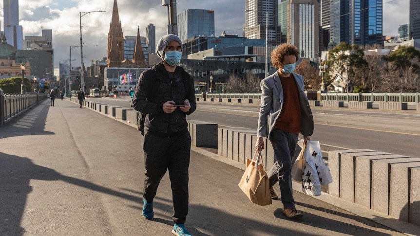 Two pedestrians in mask walk over the bridge away from the CBD. Sun is poking out behind the clouds