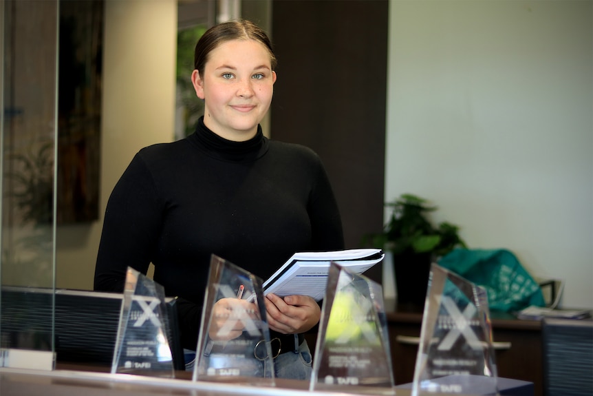 Maddie Peisley holds a book and pen with her four glass awards in front of her.