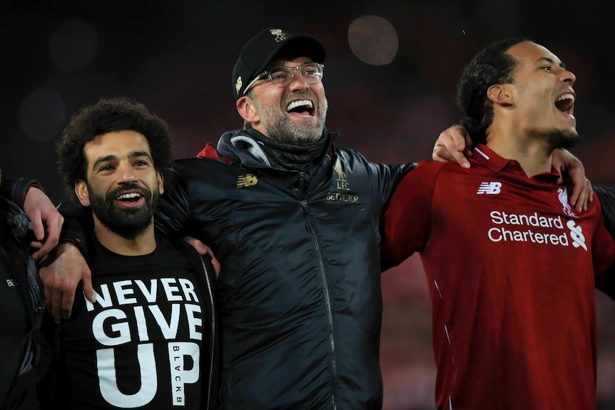 A coach and two of his players celebrate arm in arm after a football win