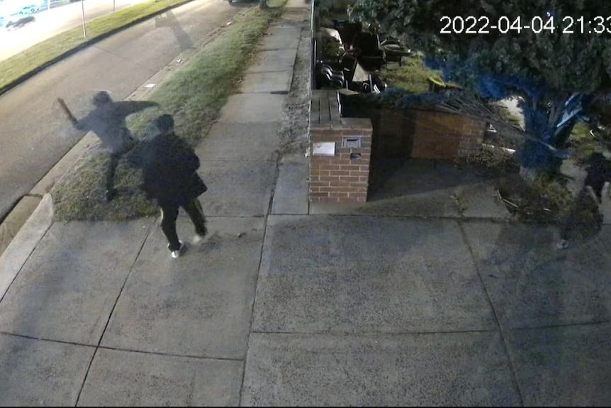 CCTV footage showing men standing on a suburban footpath at night, one of them with their arm raised.