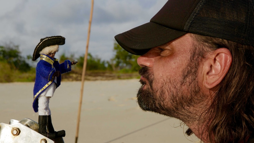 Director Warwick Thornton faces off with tiny Captain Cook puppet on a beach.