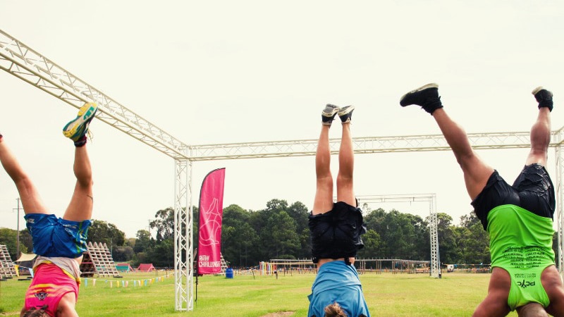 Three people doing handstands on grass wearing athletics clothes.