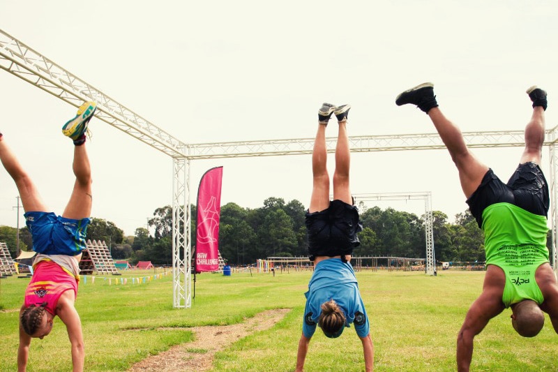 Three people doing handstands on grass wearing athletics clothes.