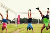 Three people doing handstands on grass wearing athletics clothes.