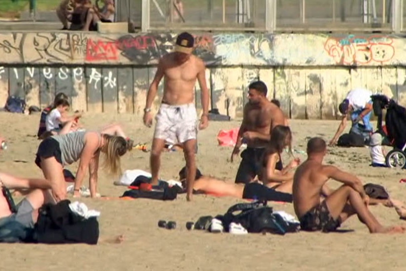 Dozens of people lounge on St Kilda beach.