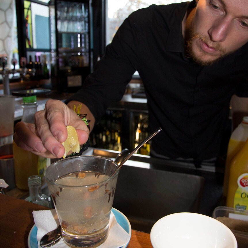 A bartender squeezes lemon into a glass of hot water with some cloves in it.