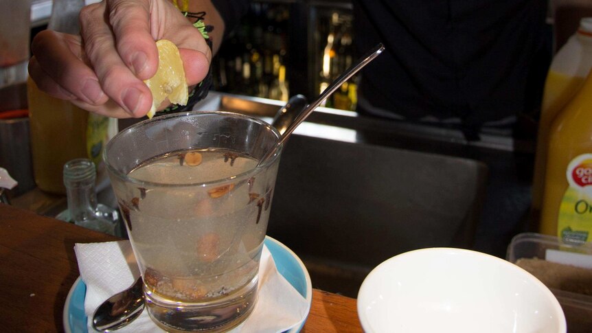 A bartender squeezes lemon into a glass of hot water with some cloves in it.