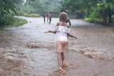 People walk in ankle-deep water down a tree-lined road.
