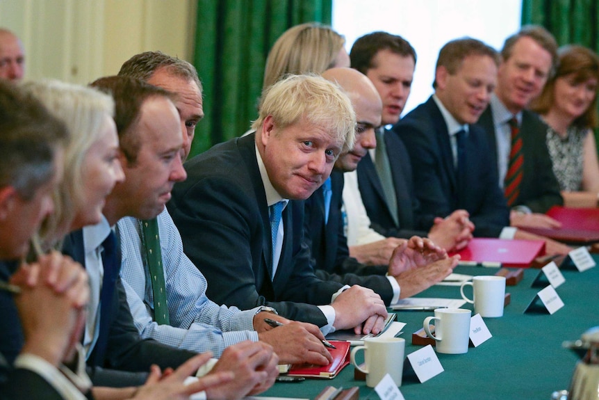 A group of Conservative Party MPs sit behind a long green table with Boris Johnson at the centre.