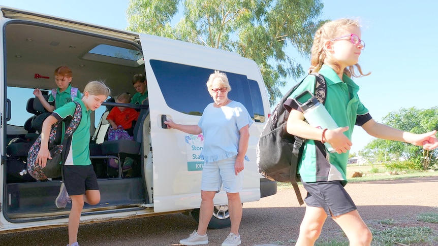 Children exit a mini-van at a primary school, as bus driver Deb holds open door