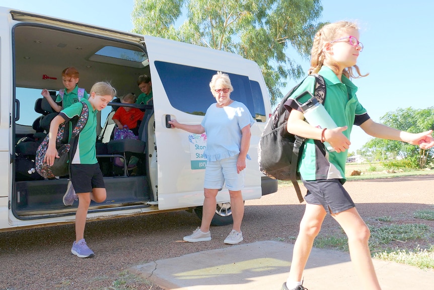 Children exit a mini van at a primary school, as bus driver Deb holds open door
