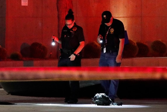 Two police officers with flashlights look down at a crime scene flooded in red light.