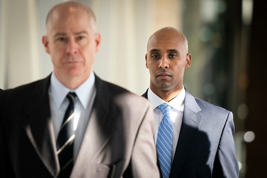 Two men in suits walk down a corridor as they depart a court