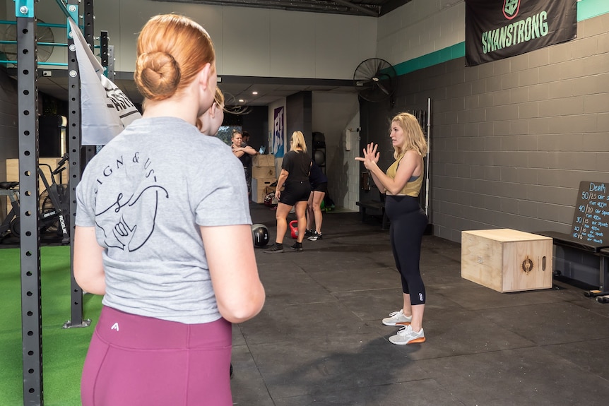 A woman signing in Auslan to a gym class of people who are deaf or hard of hearing.