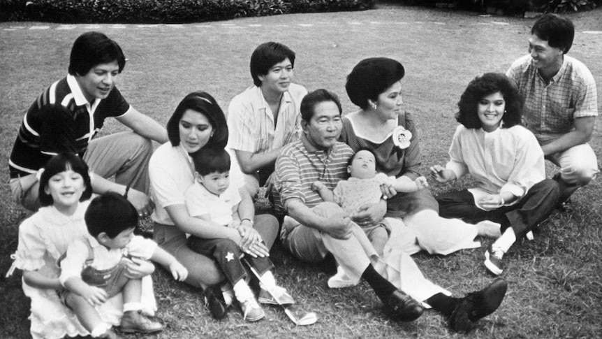 The Ferdinand family, with children, sit together on the grass in a black-and-white family photo