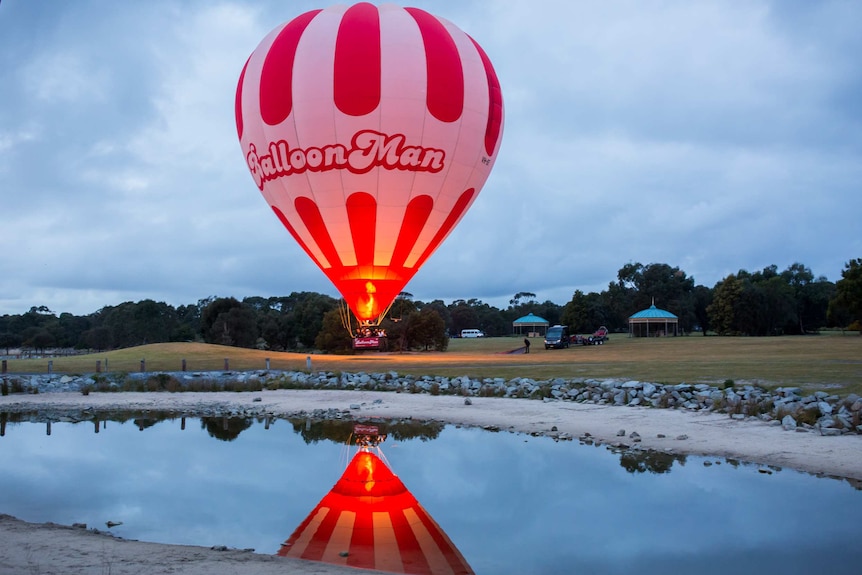 A balloon low to the ground reflects in a pond.
